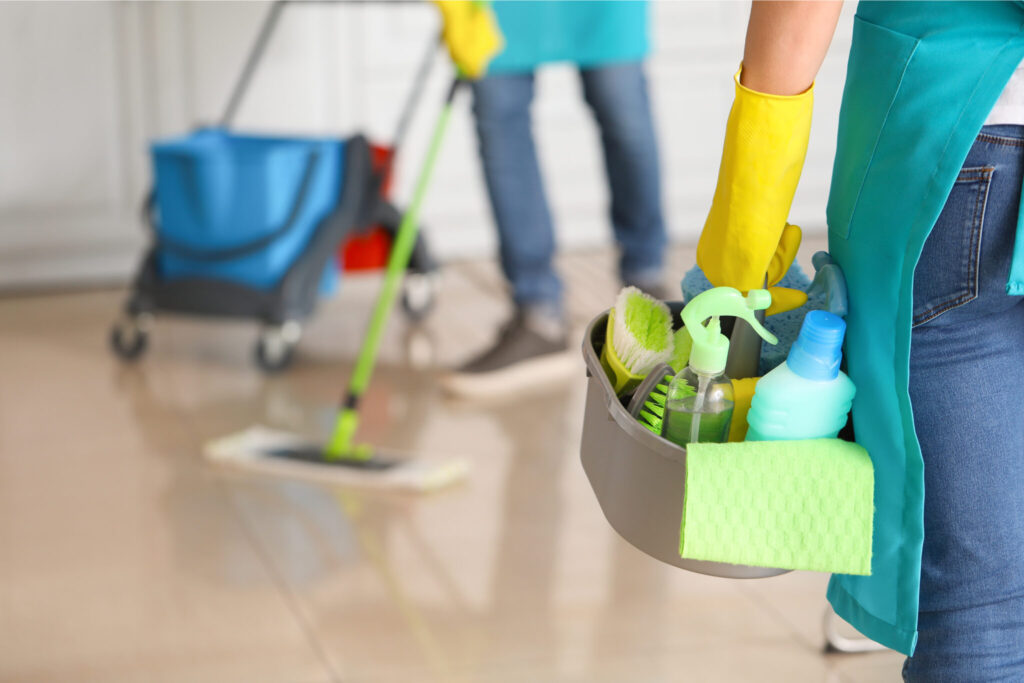 Two cleaners wearing gloves carry cleaning supplies and mop a shiny floor.