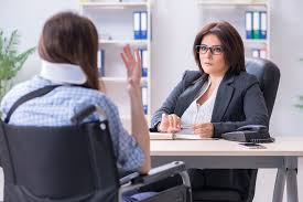 A consultant meets with a person in a wheelchair who is wearing a neck brace.