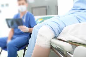 Injured patient with a bandaged knee sitting on a hospital bed.