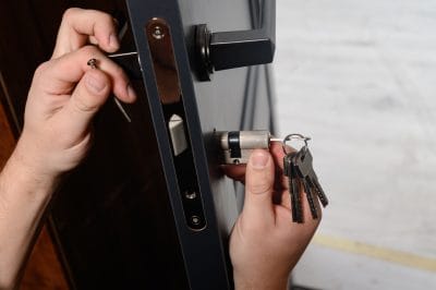 A locksmith replacing a door lock cylinder while holding a set of keys